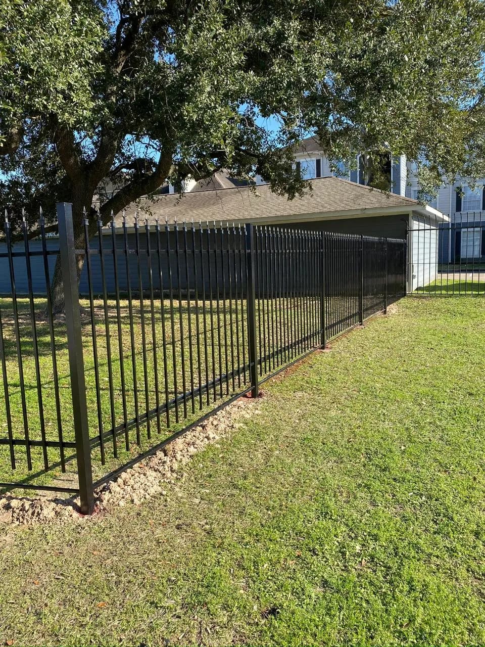 Cerca perimetral de hierro negro con puntas de lanza (spear tops) rodeando una propiedad con árboles.