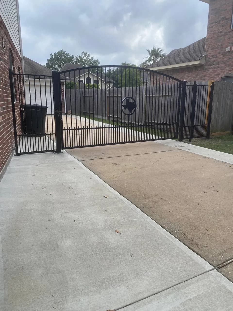 Otra perspectiva del mismo portón de file_30 (escudo de Texas) cerrado completamente, cubriendo el driveway lateral de la casa de ladrillo.