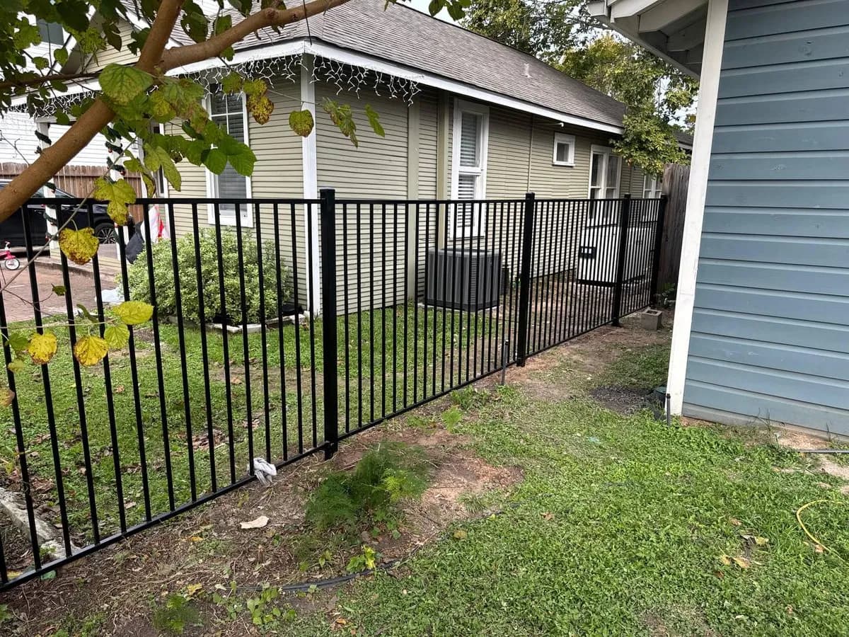 Barda separadora de hierro negro liso en el jardín lateral/trasero de una casa residencial de siding de madera verde claro.
