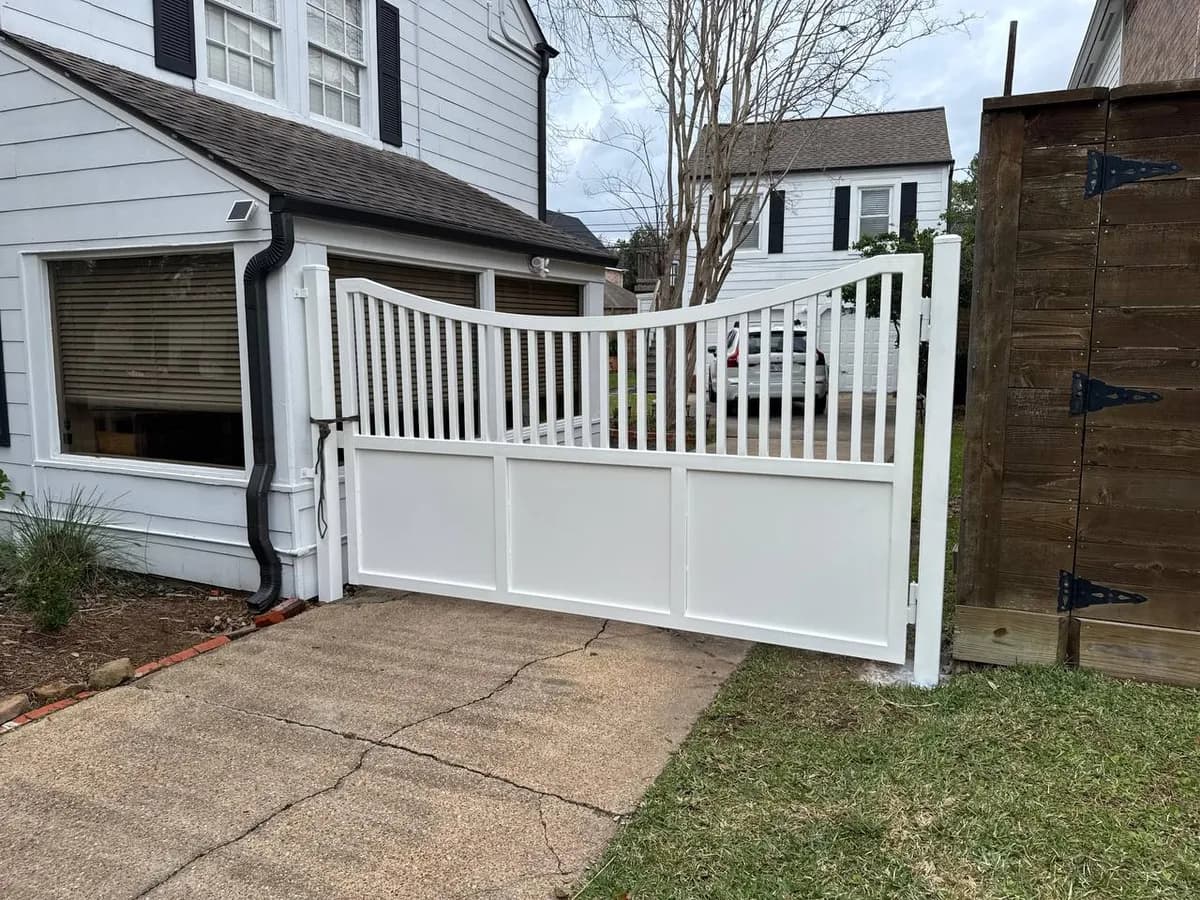 Portón de una sola hoja ancho. Color blanco sólido completo. Parte inferior opaca con paneles rectangulares y parte superior con varillas verticales. Curva elegante en el borde superior.