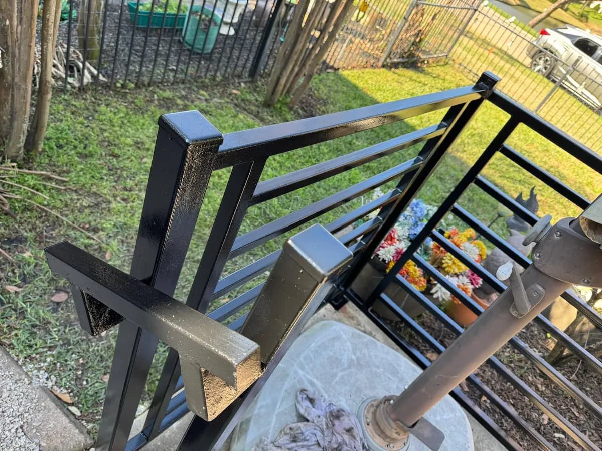 Estructura pequeña (probablemente un barandal o enclosure para patio) pintada de negro brillante (pintura fresca). Diseño de barras horizontales. Parece fabricado a medida para una base de parasol.