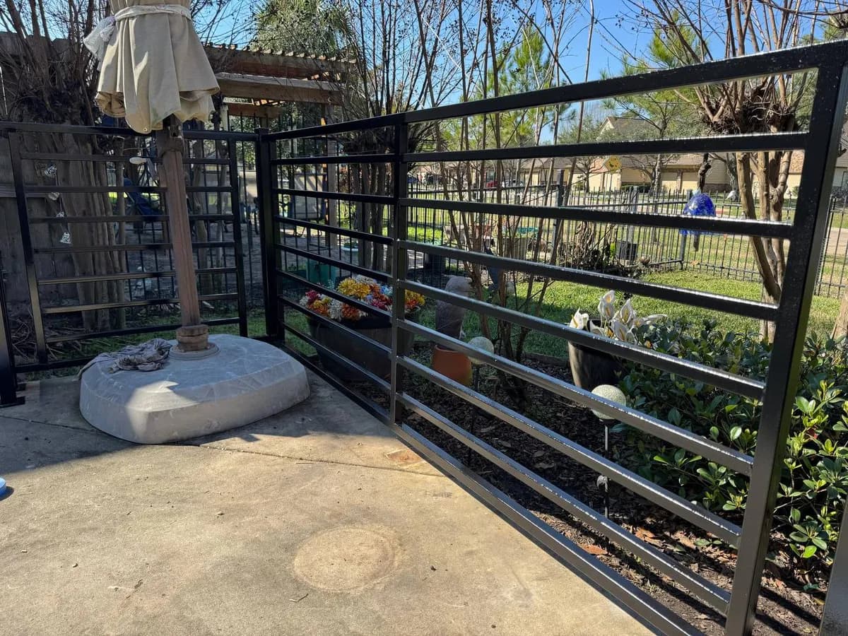 Otra toma del cercado negro de barras horizontales (file_40), protegiendo una jardinera/base de sombrilla. Diseño moderno de barras horizontales.