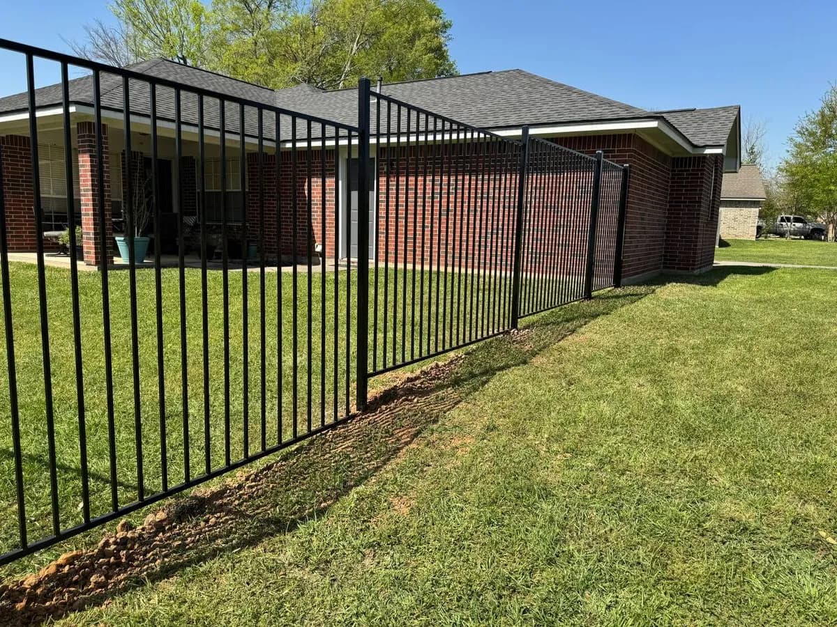 Barda perimetral negra estilo Flat Top que divide el patio de una casa de ladrillo rojo del jardín frontal/calle.
