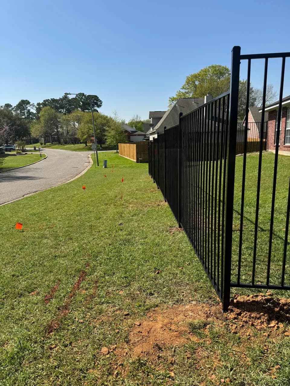 Barda esquinera de hierro negro protegiendo el jardín lateral, conectando con la pared de la casa de ladrillo. Sigue el desnivel del pasto.