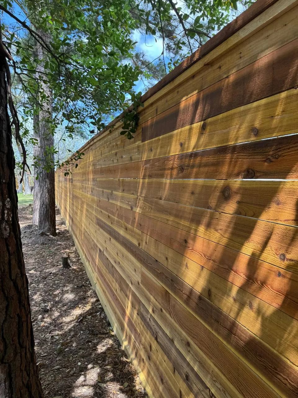 Extensión completa de la barda de tablas horizontales de madera clara. Se integra muy bien en un entorno arbolado (patio trasero).