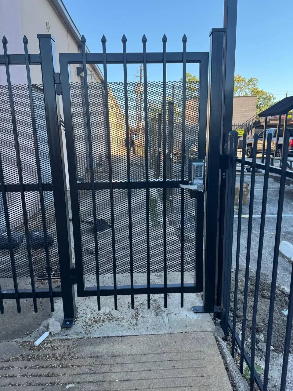 Portón peatonal de herrería con malla de metal expandido. Tiene instalada una cerradura/chapa de combinación mecánica/digital plateada. Excelente ejemplo de control de acceso comercial.