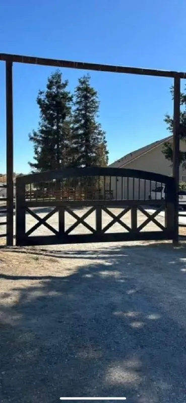 Portón de estilo rústico 'Farmhouse' (tipo establo) masivo, apoyado sobre dos vigas de metal/madera de altura exagerada. La parte baja tiene diseño de cruces (X) en repetición.