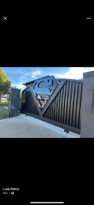 Impresionante portón deslizante con barras verticales y un escudo masivo 3D del logotipo de Superman en el centro. Ejemplo perfecto de diseño 100% personalizado.