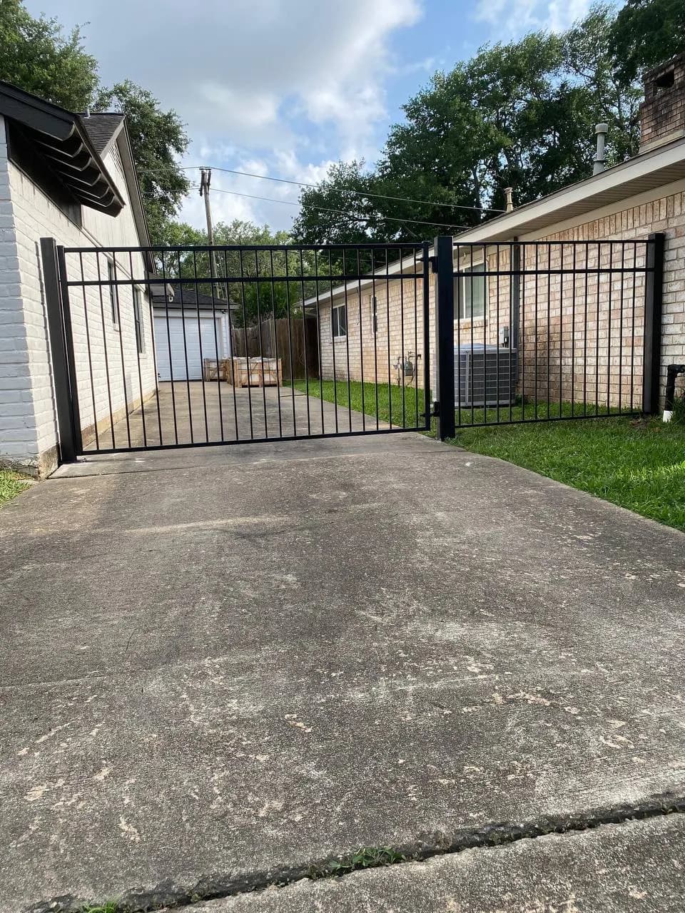 Portón deslizante recto (sin arco) de hierro negro, divide driveway de concreto entre dos casas. Diseño muy limpio y funcional.