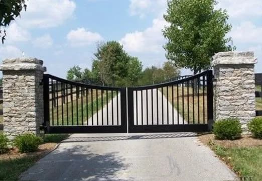 Portón doble de hierro negro con arco invertido, instalado entre columnas de piedra natural.
