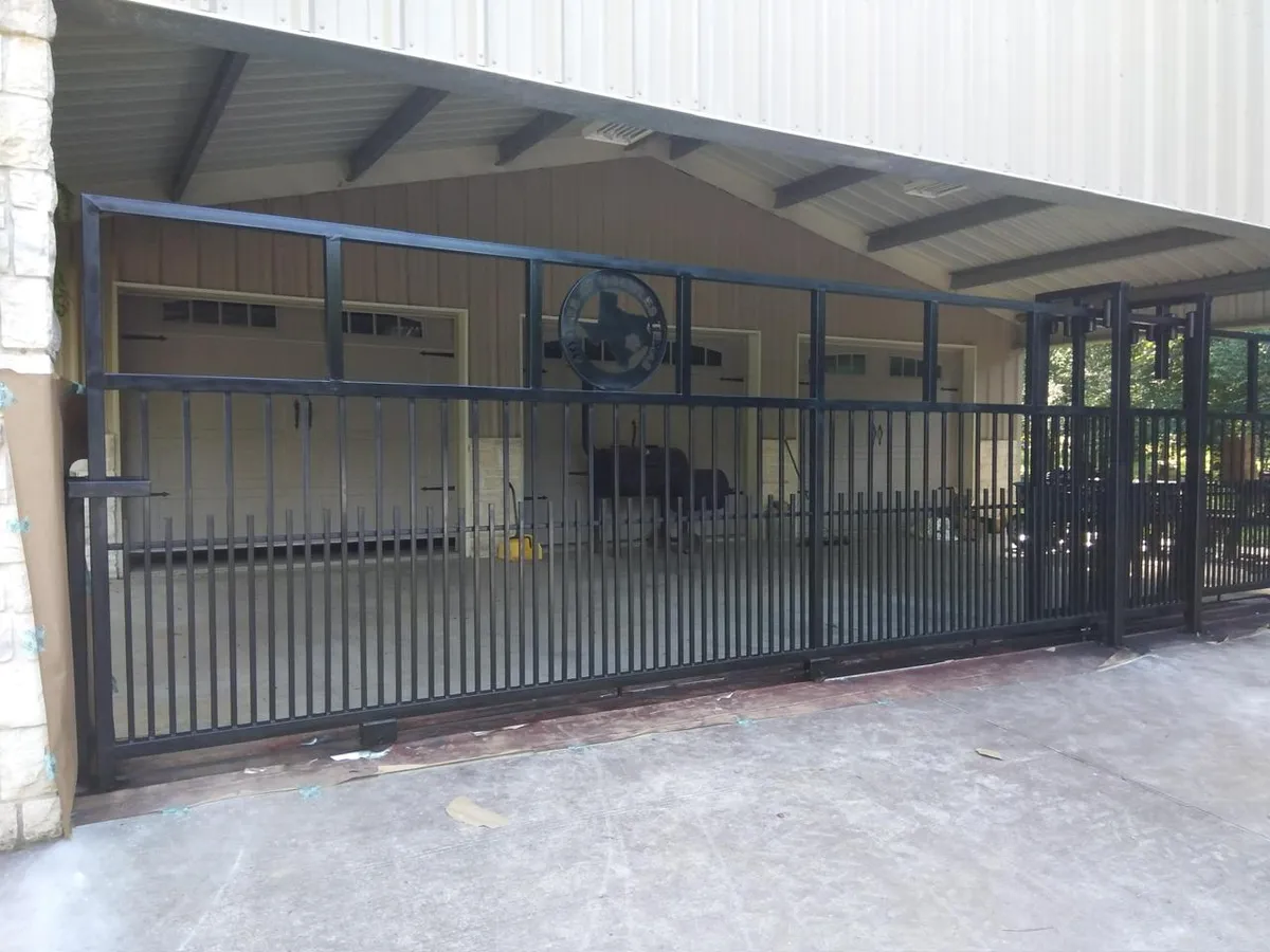 Portón deslizante masivo de hierro negro con el escudo de la estrella de Texas en el centro.