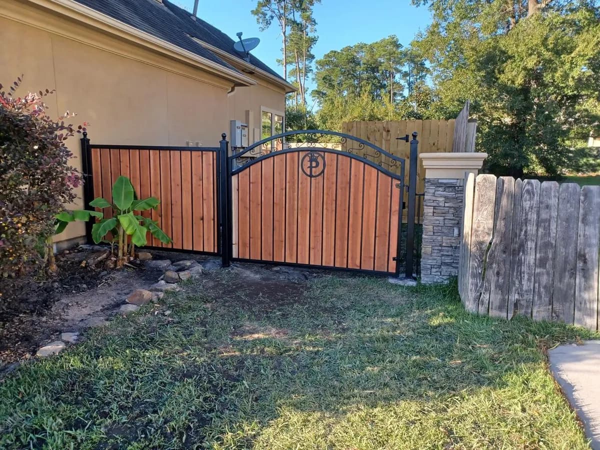 Portón de madera de cedro con marco de hierro forjado, arco superior con espirales y monograma central.