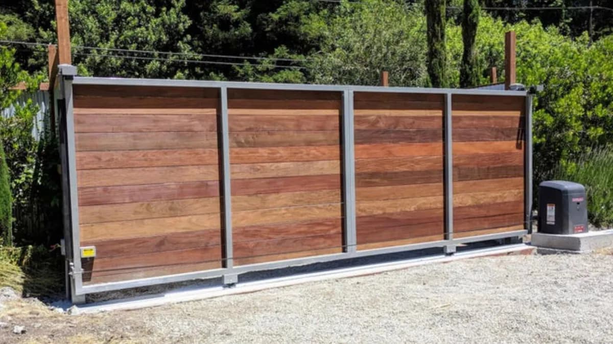 Portón deslizante automatizado de paneles de madera horizontales y marco gris.